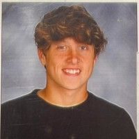 A young man in a black shirt smiling in a portrait photograph.