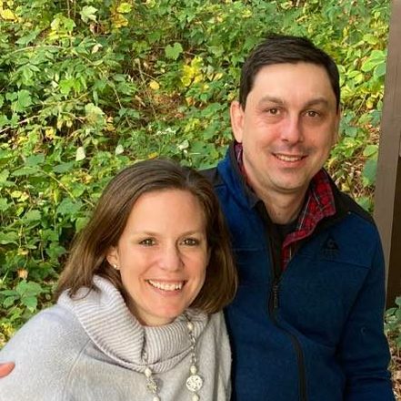 A man and a woman are posing for a picture in the woods.