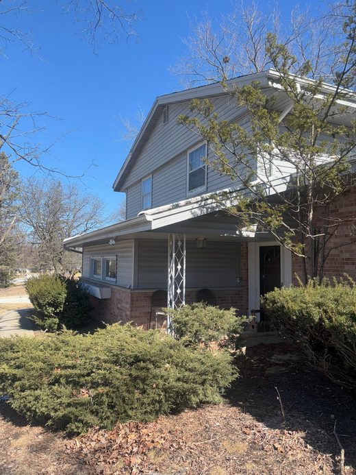 A two storey house with a covered porch and shrubs in the front garden.