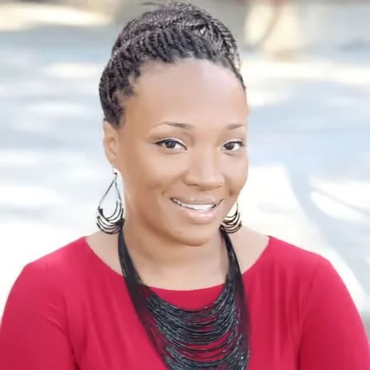 A woman in a red top with large earrings is smiling outdoors.