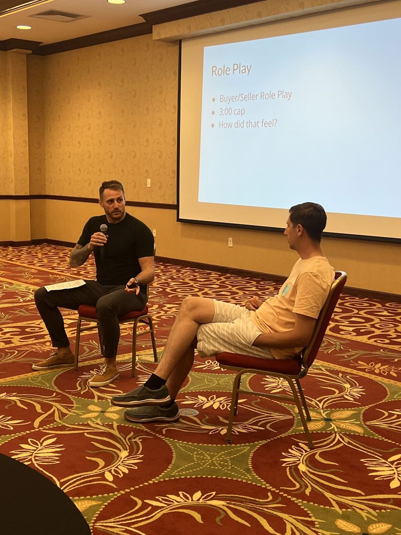 Two men are sitting in chairs talking in front of a projector screen