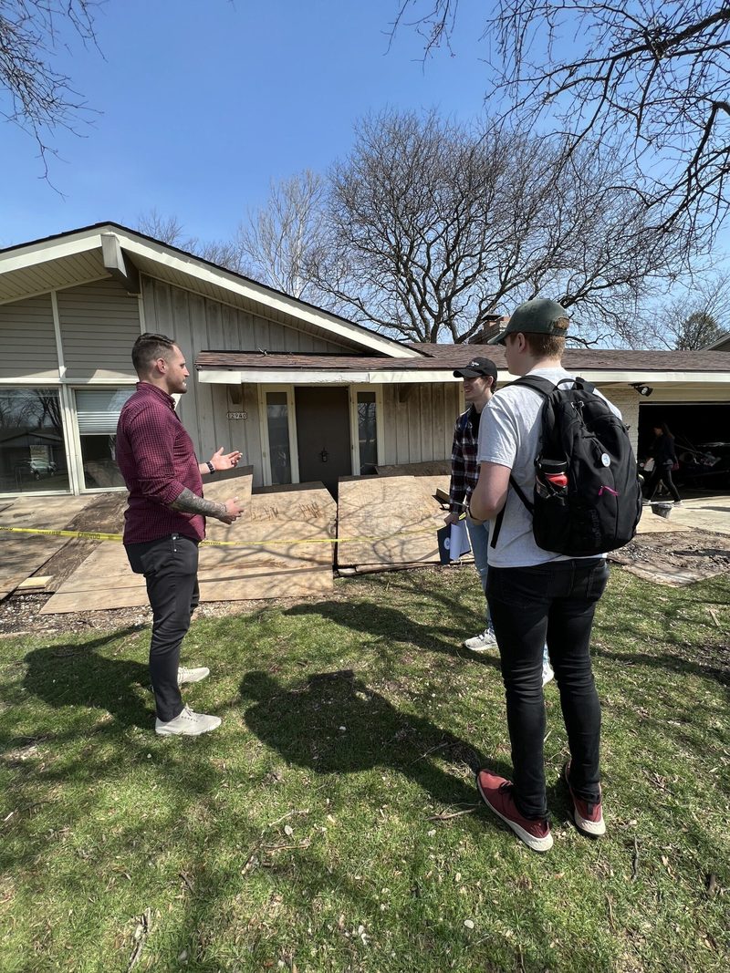 Three men are standing in front of a house talking to each other