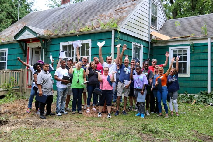 A group of people are standing in front of a green house.