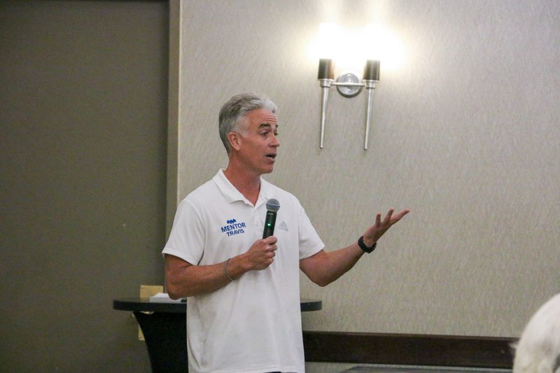 A man in a white shirt is holding a microphone in a room.