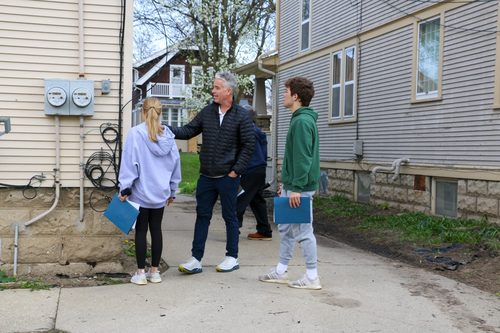 A group of people are standing on a sidewalk in front of a building.