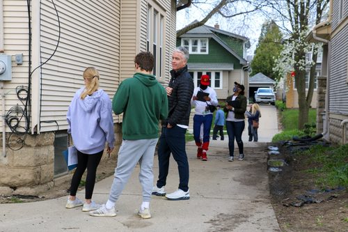 A group of people are standing on a sidewalk in front of a house.