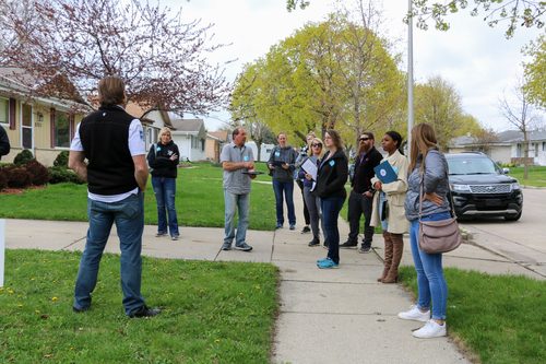 A group of people are standing on a sidewalk in front of a house.