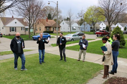 A group of people are standing on a lush green lawn in a residential neighborhood.