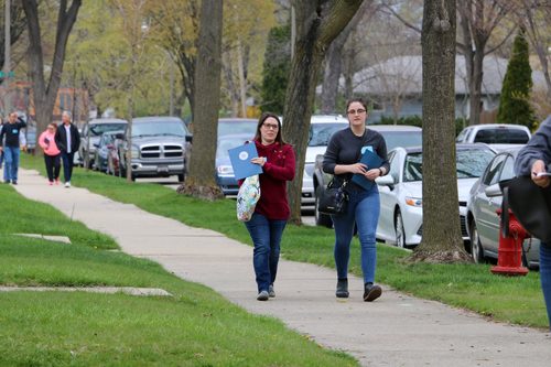 A group of people are walking down a sidewalk in a residential neighborhood.