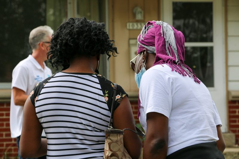 Two women wearing face masks are standing in front of a house.