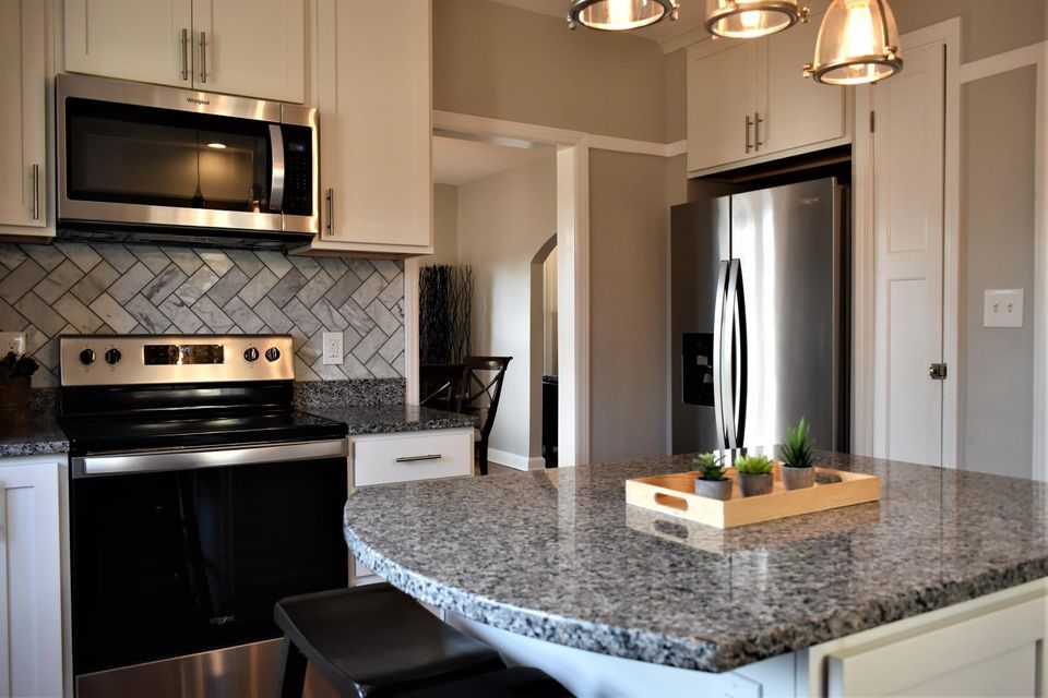 A kitchen with granite counter tops , stainless steel appliances , and white cabinets.