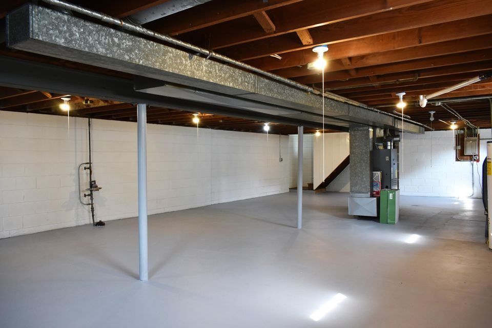 An empty basement with white walls and a wooden ceiling.