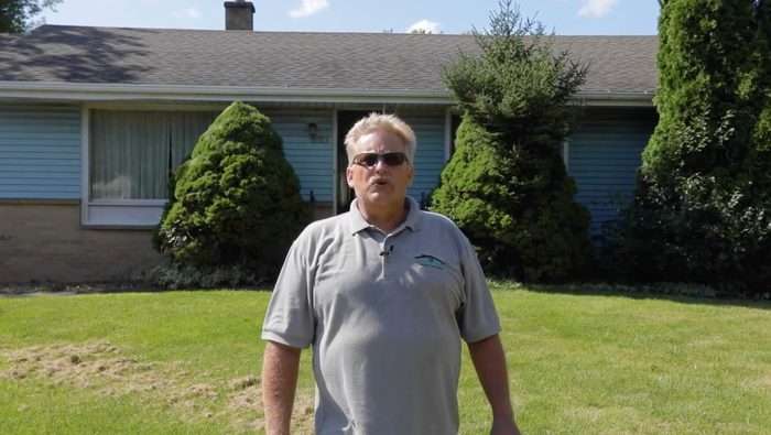 A man wearing sunglasses is standing in front of a house.