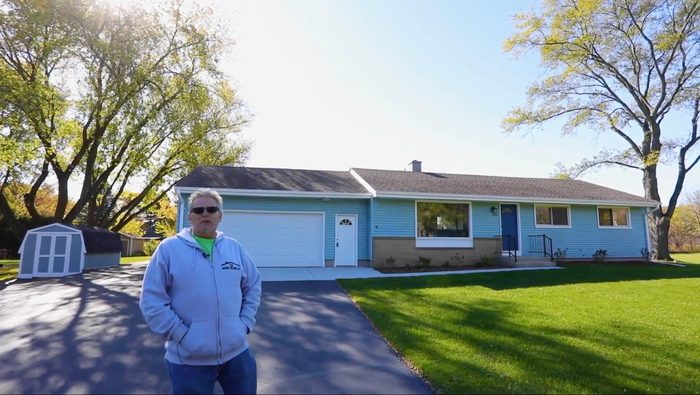 A man is standing in front of a blue house.